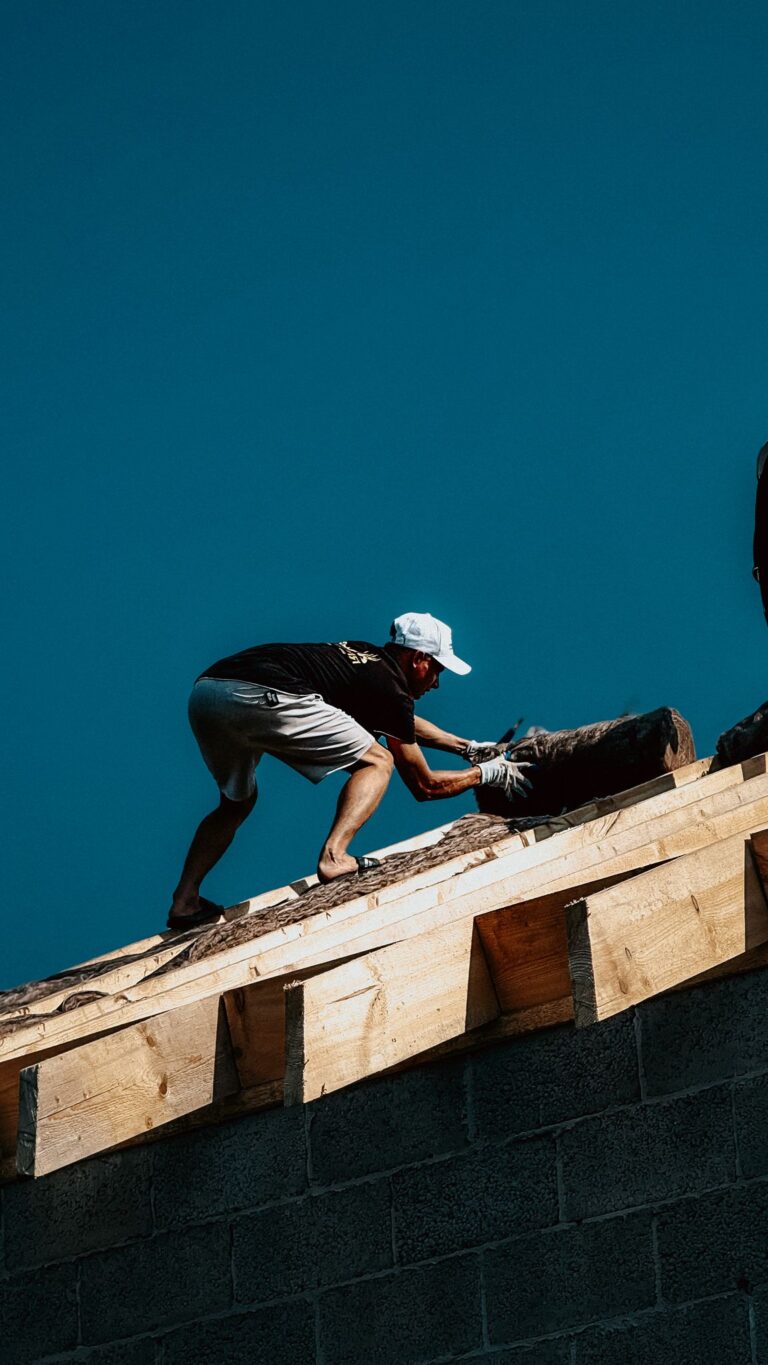 A construction worker actively working on roofing under a clear blue sky, showcasing manual labor and building expertise.